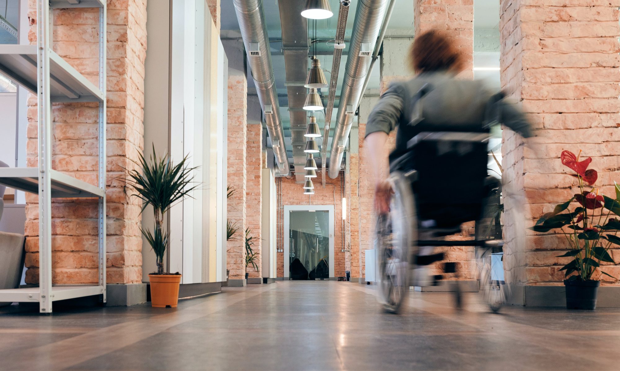 An image inside a large office space with a wheelchair user moving away (and the person is blurred)